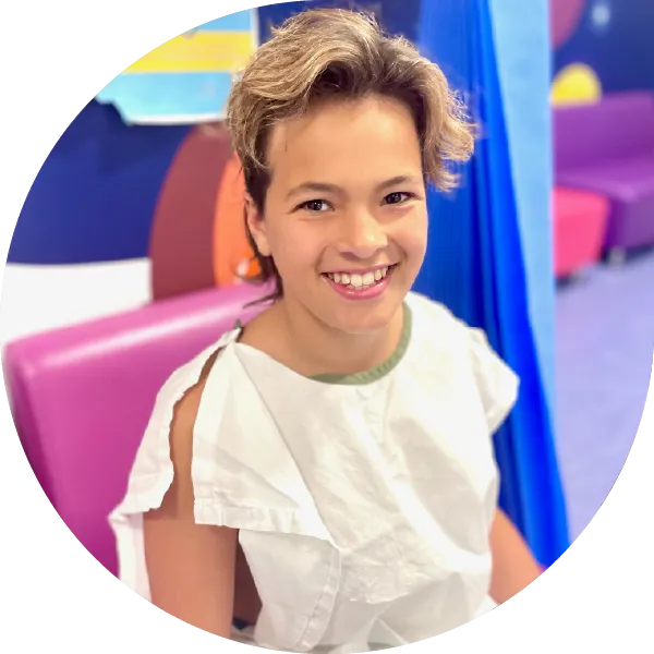 Remy smiling while wearing a hospital gown, sitting in a hospital waiting room